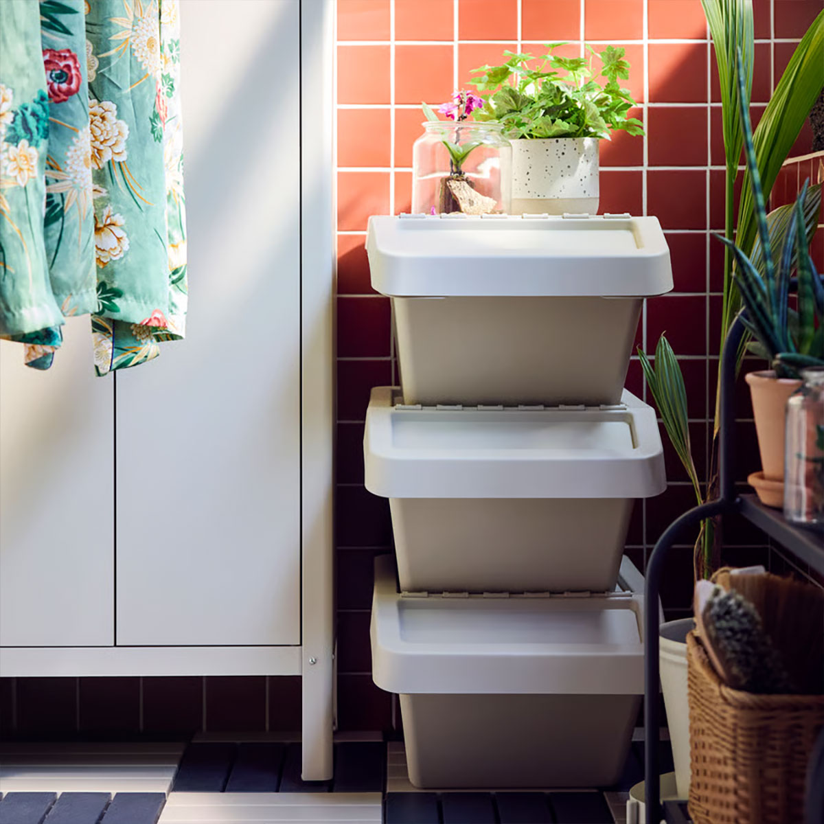 A balcony with a beige KOLBJÖRN cabinet for storage, featuring baskets and cleaning supplies. Indoor plants are nearby.
