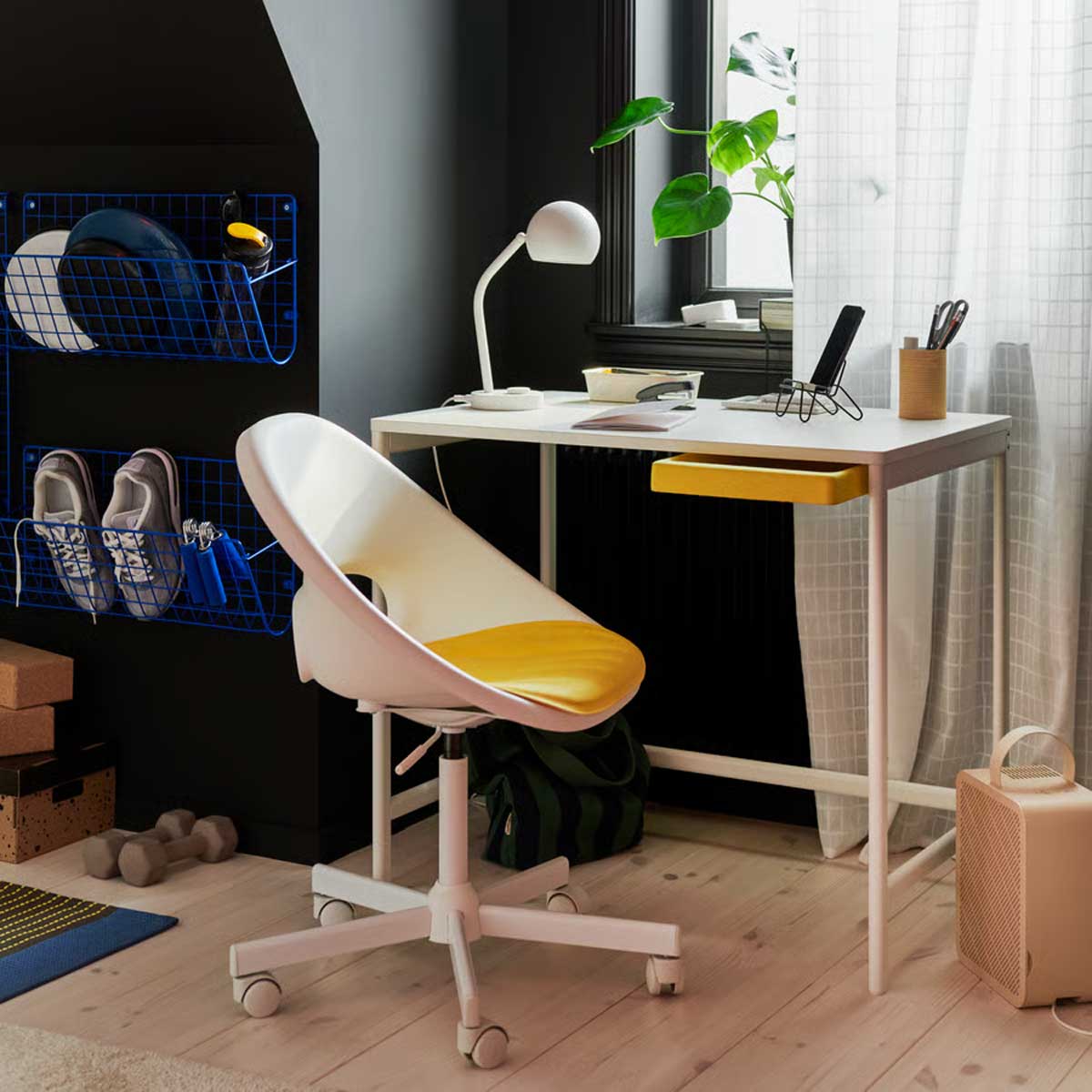 A study area with a white ENKROKEN desk and a white LOBERGET chair. A plant sits on the desk, beside shelves on a dark wall.