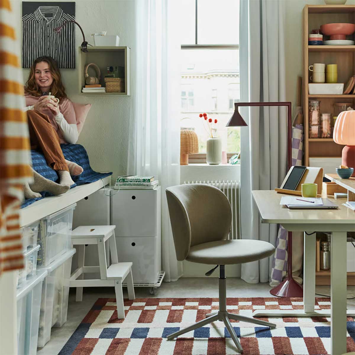 A dorm room includes a dark beige KRYLBO swivel chair made from Tonerud, in front of a height-adjustable desk.