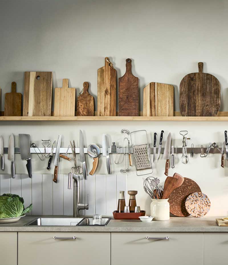 A light-coloured kitchen with narrow shelves holding wooden cutting boards and KUNGSFORS magnetic knife racks.