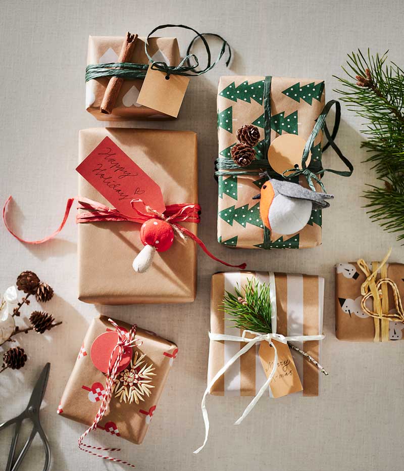 Six gifts wrapped in VINTERFINT wrapping paper, personalised with tree ornaments, a cinnamon stick and pine cones.