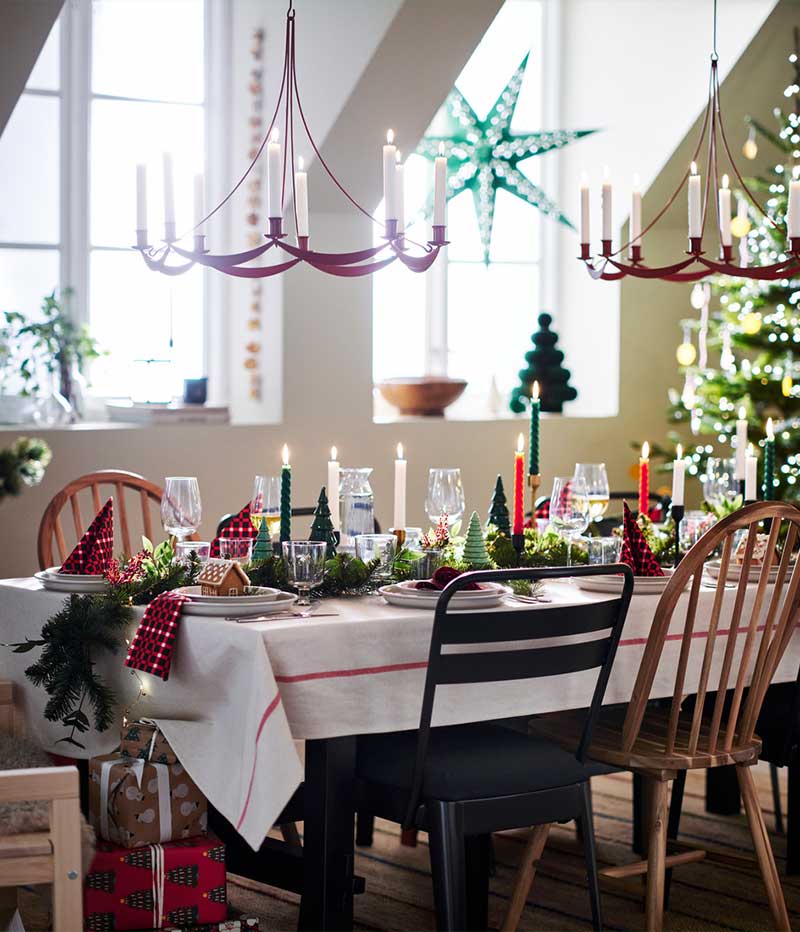 A dining table set for a Christmas meal with a green and red theme and two VINTERFINT chandeliers above.