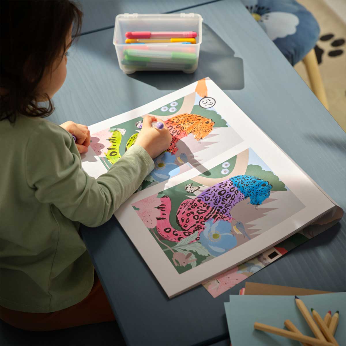 A child colours a leopard in the ALPTALL activity book which has colouring pages and games.