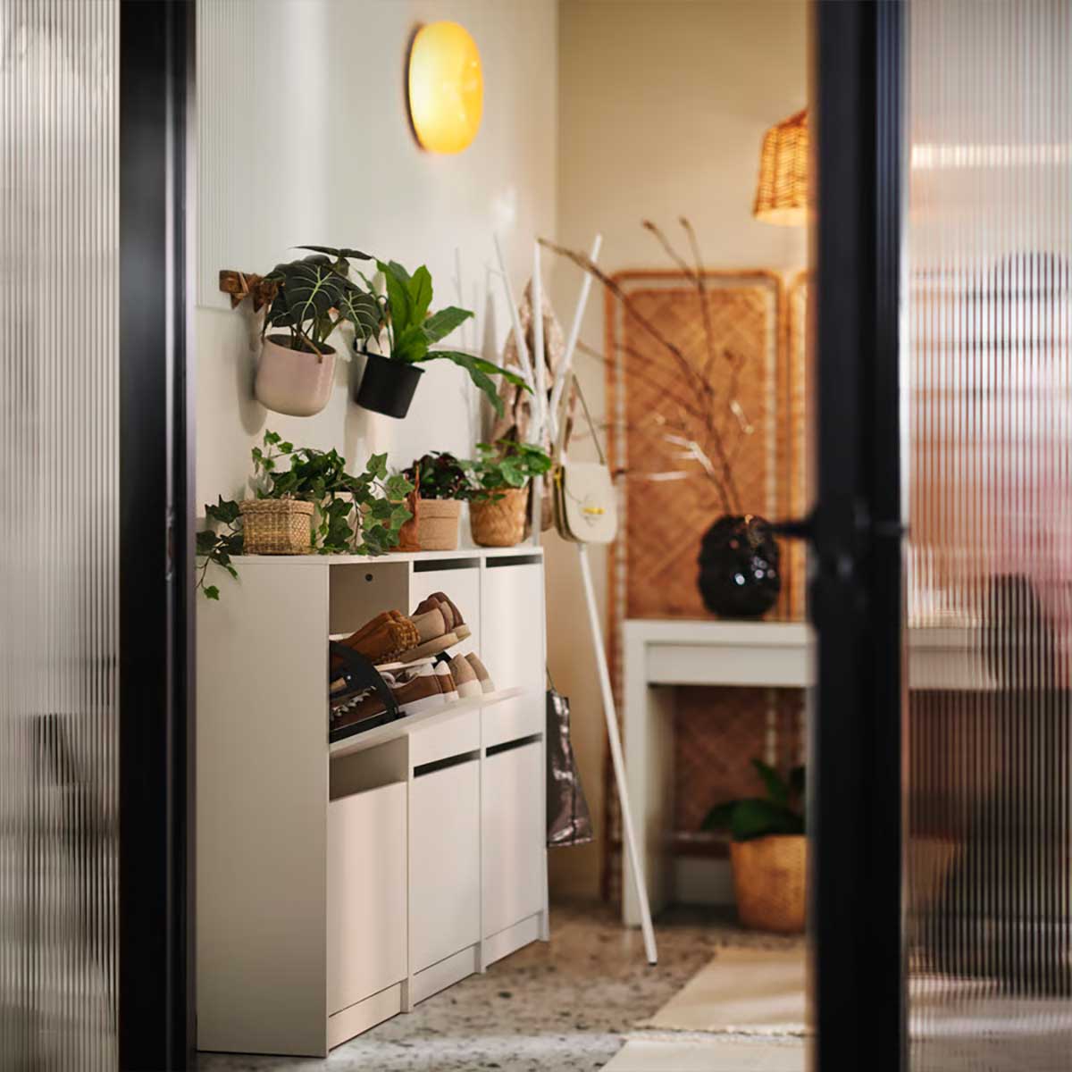 Three BISSA shoe cabinets side by side in a cosy hallway with plants in pots on top and a round VARMBLIXT wall lamp above.