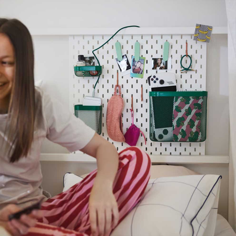 A SKÅDIS pegboard attached to a fourposter bed, being used with green SKÅDIS  accessories such as baskets and clips.